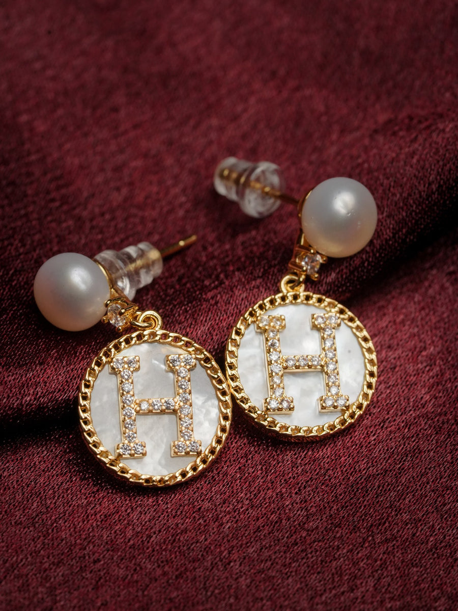Ashborne Ishita pearl-top drop earrings with mother-of-pearl H initial discs on burgundy