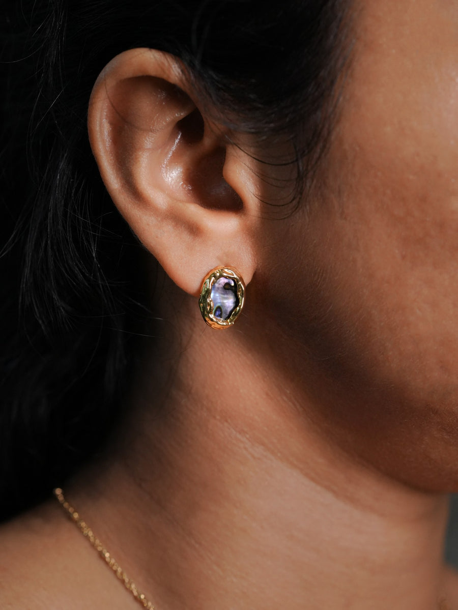 Ashborne Eela abalone oval stud earring with rippled gold-tone bezel, worn on ear