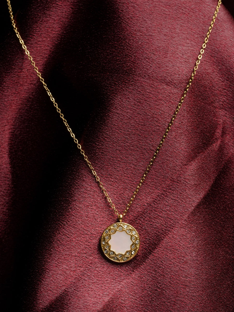 Ashborne Pari sunburst mother-of-pearl medallion necklace worn on maroon satin